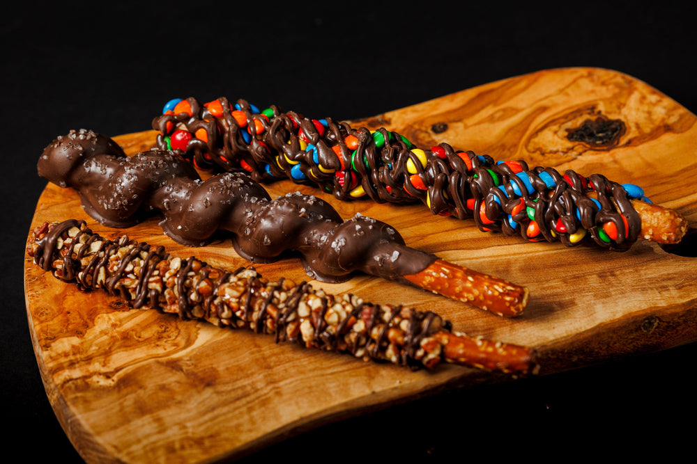 A selection of gourmet pretzels with various toppings, including nuts and candies, displayed on a wooden board.
