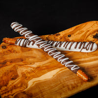 Pretzel rods with white and dark chocolate drizzles on top, placed on a wooden surface.