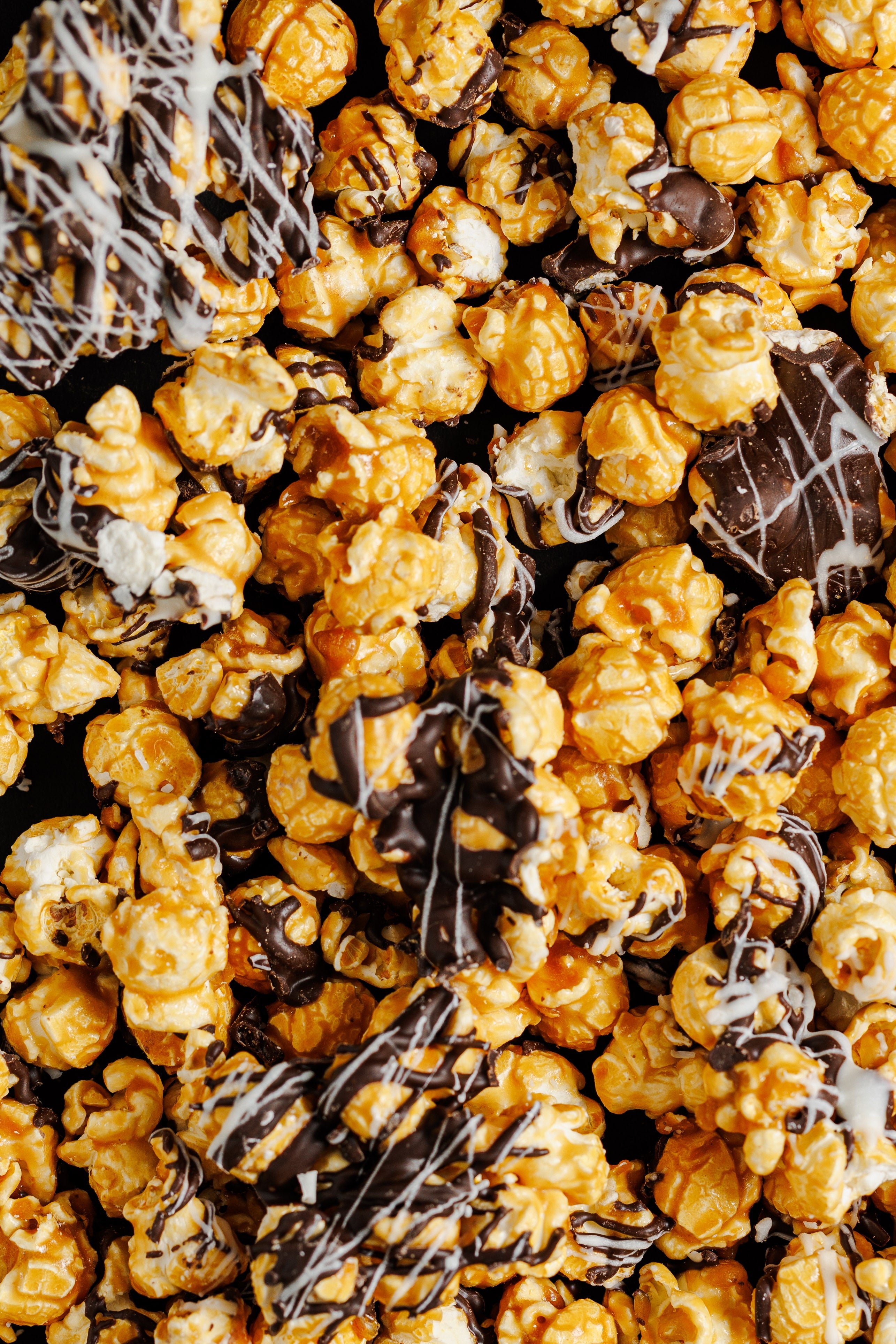 A close-up, top-down view of caramel popcorn chunks drizzled with dark & white chocolate, filling the entire frame.