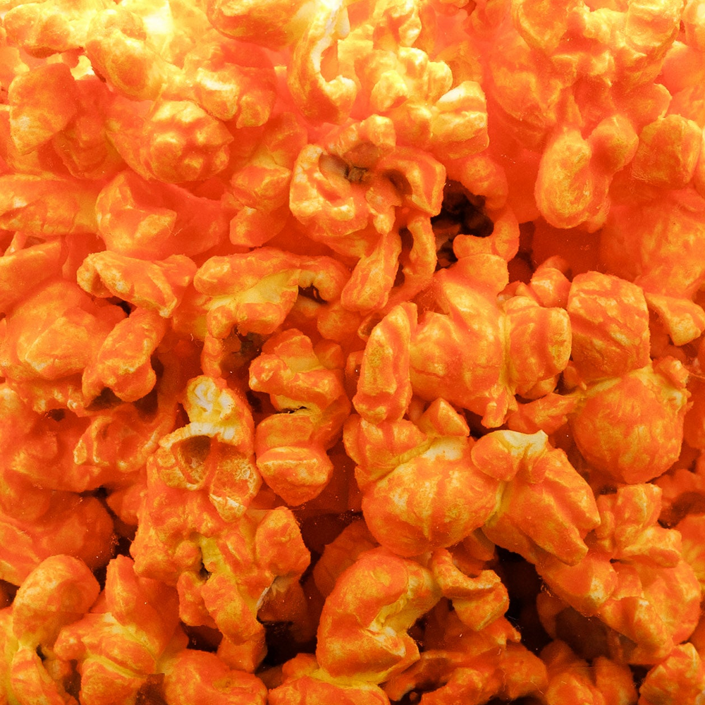 A close-up, top-down view of glistening, glossy orange popcorn kernels filling the entire frame.