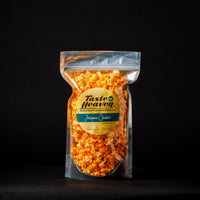 A sealed clear plastic bag of Taste of Heaven brand Jalapeño Cheddar Cheese flavored popcorn. The popcorn is orange from the cheese coating, and the packaging has a green label with the product name and branding.