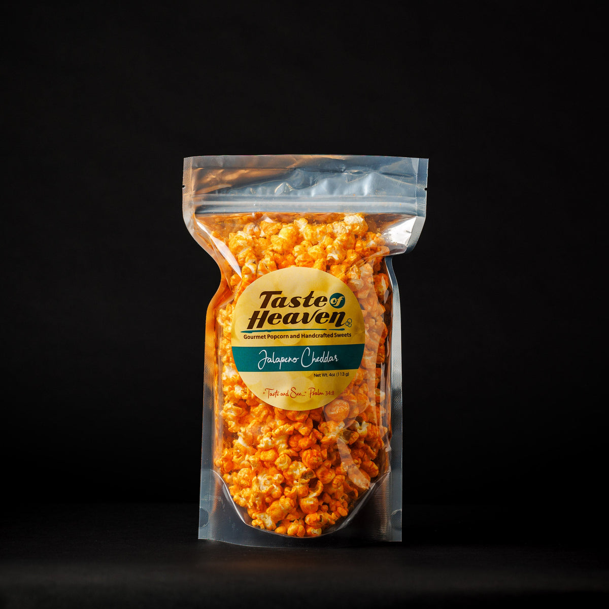 A sealed clear plastic bag of Taste of Heaven brand Jalapeño Cheddar Cheese flavored popcorn. The popcorn is orange from the cheese coating, and the packaging has a green label with the product name and branding.