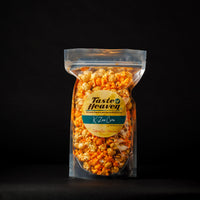 A clear stand-up pouch filled with orange-topped popcorn, centered on a black background. The front label reads Taste Heaven and K-Zoo Corn.