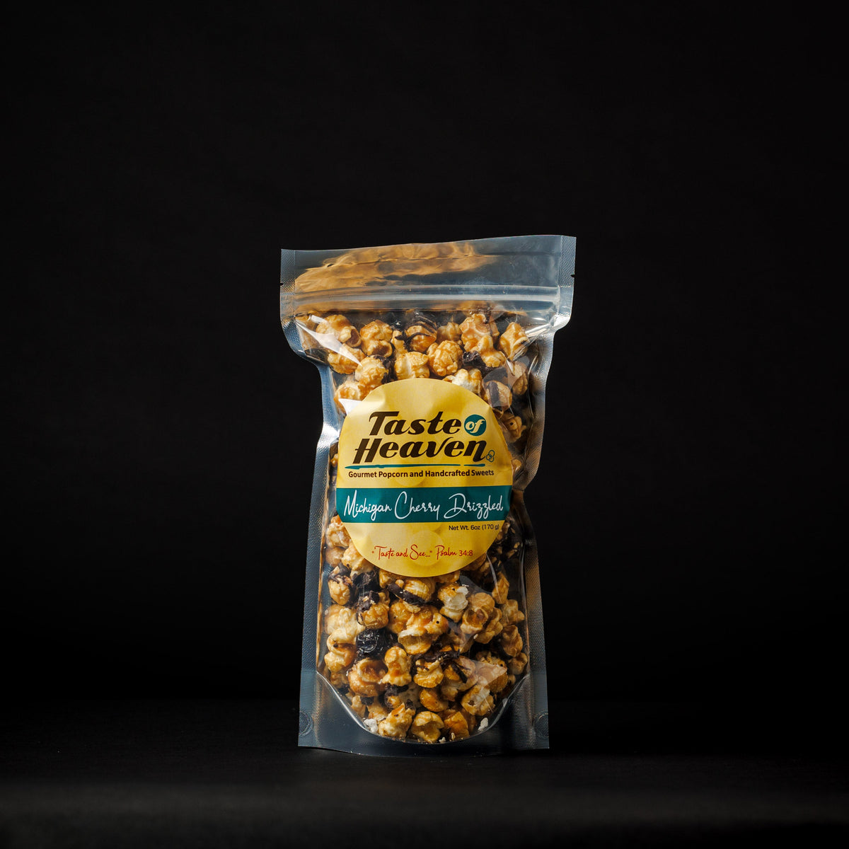 A clear stand-up pouch of Tasted Heaven Michigan Cherry Drizzled bag filled with popcorn, set against a solid black background.