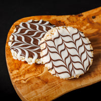 A chocolate-coated crisped rice treat with a pattern of white chocolate swirls on a wooden board.
